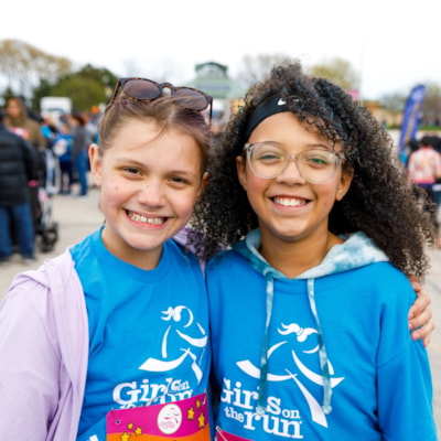 Two girls in yellow Girls on the Run shirts embrace with smiles